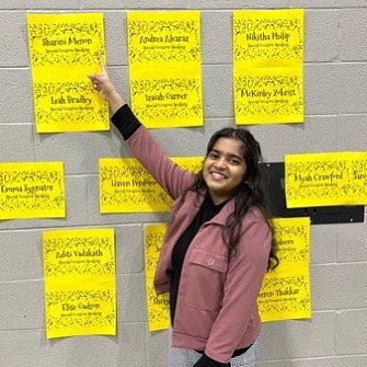 Sharini Menon points to a sign that says her event, Special Occasion Speaking, at the 2023 IHSA State Finals. This is her first time qualifying for State.
